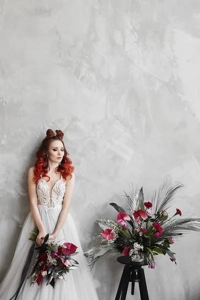 Fashionable portrait of a model girl with red hair and trendy makeup in a wedding dress posing with bridal bouquet — Stock Photo, Image