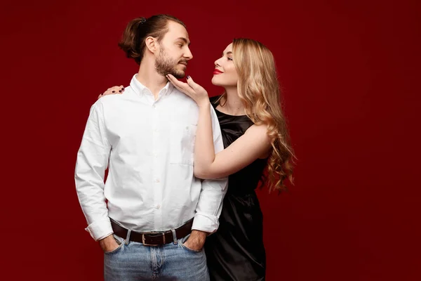 Um casal encantador, uma mulher bonita com cabelo loiro e um homem bonito posando no fundo vermelho — Fotografia de Stock