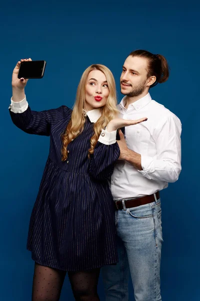 Eine hübsche blonde Frau macht ein Selfie mit einem hübschen jungen Mann im blauen Hintergrund lizenzfreie Stockbilder