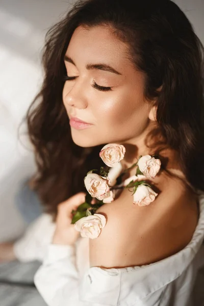 Eine junge kaukasische Model-Frau mit sanftem Make-up posiert mit Blumenzweigen vor weißem Hintergrund. Model Mädchen mit Rosenzweig Stockbild