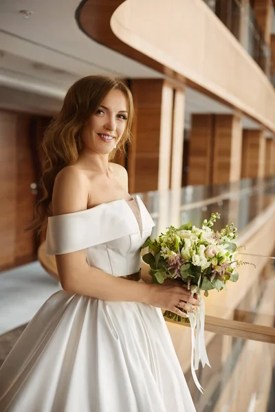 Glückliche junge Frau im modischen Hochzeitskleid posiert mit einem wunderschönen Brautstrauß Stockbild