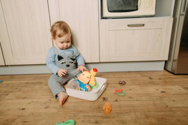kid sits inside on the floor the kitchen plays with bright toy