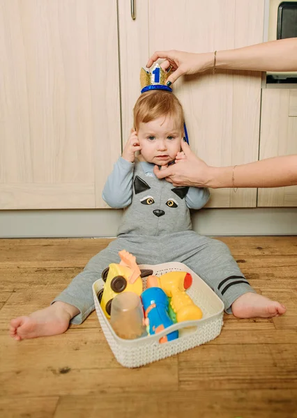 kid sits inside on the floor the kitchen plays with bright toy