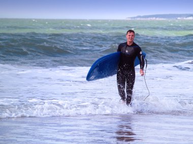 Sahilde yürüyen bir sörfçü.