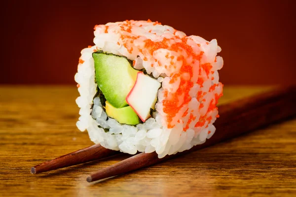 Uramaki sushi closeup on chopsticks — Stock Photo, Image
