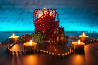 Hediye kutuları, mum ışıkları, kırmızı ve altın rengi Noel süslemeleri mavi arka planda.