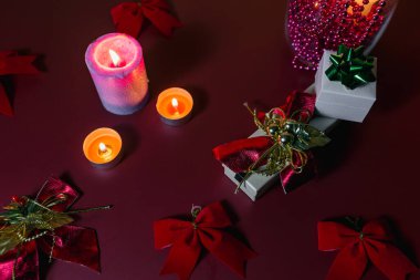 Noel sofrasında mumlar ve kırmızı arka planda hediyeler.