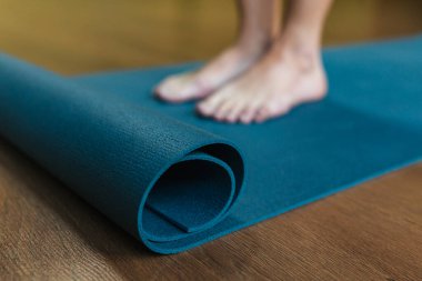 Bir kız mavi yoga minderinin yanında duruyor..