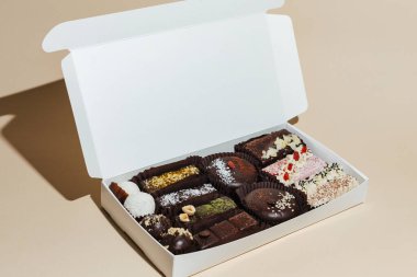 Sarı arka plandaki hediye kutusunda çeşitli el yapımı vejetaryen çikolata şekerlemeleri var.