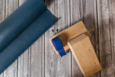 Ahşap zeminde iki ahşap yoga bloğu, kemer ve mavi yoga minderi var. Fitness, esneme ve gevşeme.