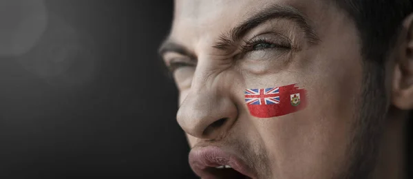 A screaming man with the image of the Bermuda national flag on his face — Stock Photo, Image