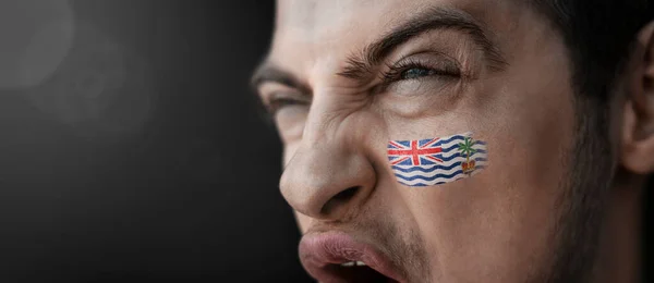 Un hombre gritando con la imagen de la bandera nacional del Territorio Británico del Océano Índico en su cara — Foto de Stock