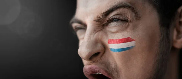 Um homem gritando com a imagem da bandeira nacional do Luxemburgo em seu rosto — Fotografia de Stock