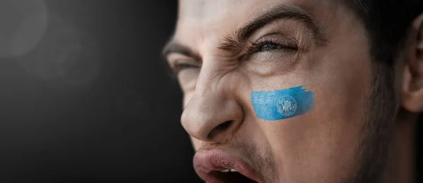 Un homme criant à l'image du drapeau national de l'Organisation internationale de la propriété intellectuelle sur son visage — Photo