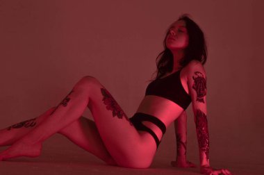 Erotik kız iç çamaşırlarıyla yerde ve pembeyle oturuyor.