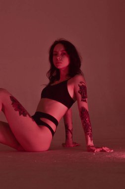 Erotik kız iç çamaşırlarıyla yerde ve pembeyle oturuyor.