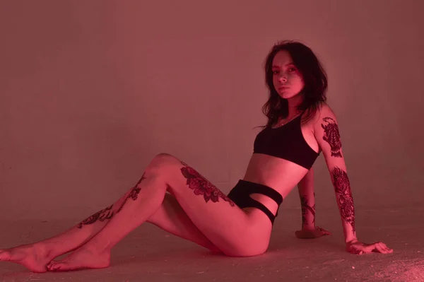 Erotik kız iç çamaşırlarıyla yerde ve pembeyle oturuyor.