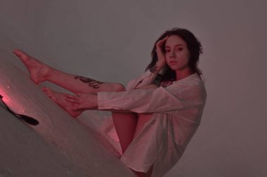 Beyaz tişörtlü erotik kız pembe neonlu yerde oturuyor.