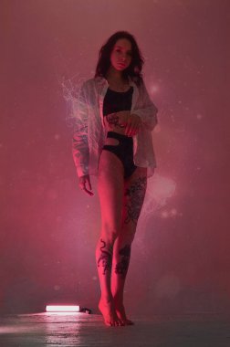 İç çamaşırlı erotik kız pembe neon ışıkta duruyor.