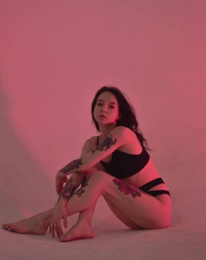 Erotik kız iç çamaşırlarıyla yerde ve pembeyle oturuyor.