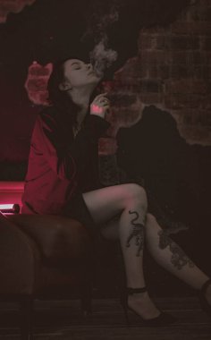 Ceketli ve seksi bir kız kırmızı neonlu sigara içiyor.