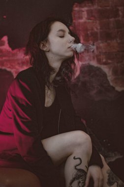 Ceketli ve seksi bir kız kırmızı neonlu sigara içiyor.