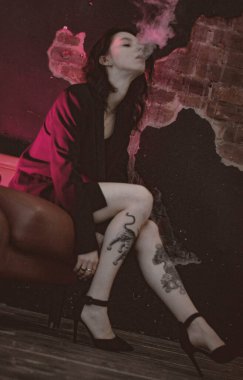 Ceketli ve seksi bir kız kırmızı neonlu sigara içiyor.