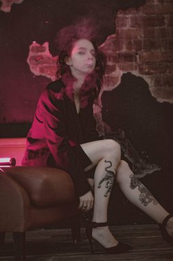 Ceketli ve seksi bir kız kırmızı neonlu sigara içiyor.