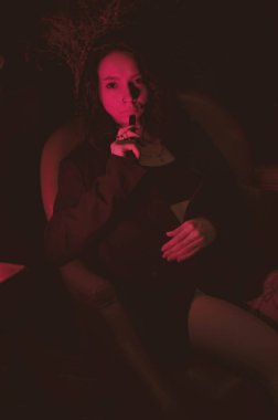 Ceketli ve seksi bir kız kırmızı neonlu sigara içiyor.
