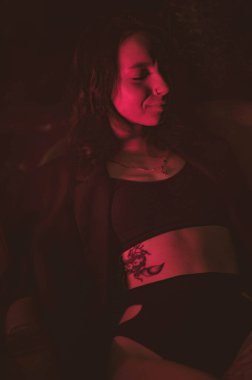 Ceketli ve seksi bir kız kırmızı neonlu sigara içiyor.