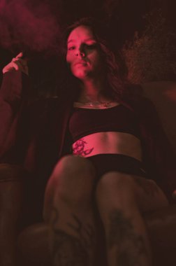 Ceketli ve seksi bir kız kırmızı neonlu sigara içiyor.