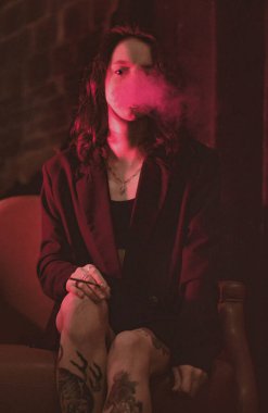 Ceketli ve seksi bir kız kırmızı neonlu sigara içiyor.