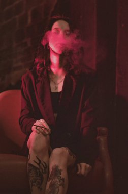 Ceketli ve seksi bir kız kırmızı neonlu sigara içiyor.