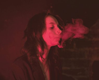 Ceketli ve seksi bir kız kırmızı neonlu sigara içiyor.