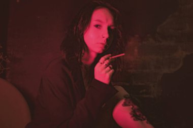 Ceketli ve seksi bir kız kırmızı neonlu sigara içiyor.
