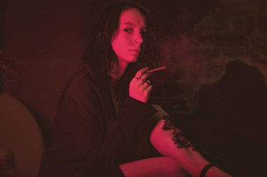 Ceketli ve seksi bir kız kırmızı neonlu sigara içiyor.