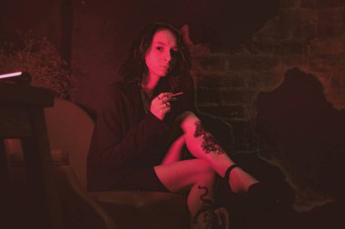 Ceketli ve seksi bir kız kırmızı neonlu sigara içiyor.