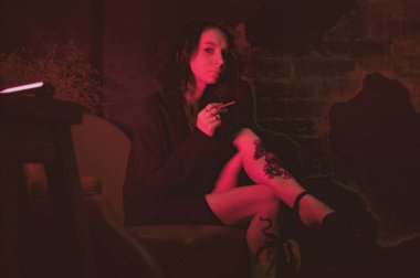 Ceketli ve seksi bir kız kırmızı neonlu sigara içiyor.