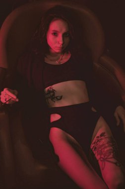 Ceketli ve seksi bir kız kırmızı neonlu bir koltukta yatıyor.