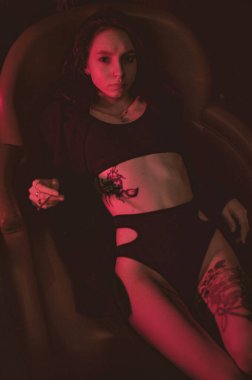 Ceketli ve seksi bir kız kırmızı neonlu bir koltukta yatıyor.