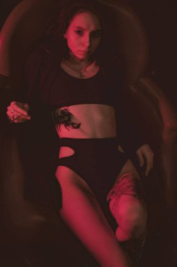 Ceketli ve seksi bir kız kırmızı neonlu bir koltukta yatıyor.