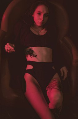 Ceketli ve seksi bir kız kırmızı neonlu bir koltukta yatıyor.