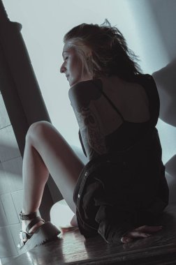 Güneşli bir odada siyah saçlı ve şortlu bir kız.