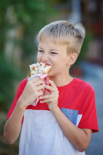 Lindo chico rubio comiendo rollo de camarones en el restaurante de comida rápida. Comida poco saludable para los niños. Comida chatarra. — Foto de Stock