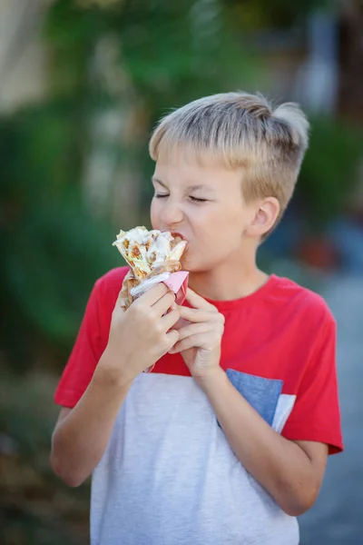 Netter blonder Junge isst Shrimp Roll im Fast-Food-Restaurant. Ungesunde Mahlzeiten für Kinder. Junk food. — Stockfoto