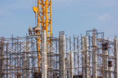 Kova sıvı beton konteynırla boy ekipmanında çalışıyor. İnşaat işçisi yüksek bir binada çalışıyor. Crane, çimento karıştırma makinesini bir binaya taşıyor. Turna asansörü beton karıştırıcı kap