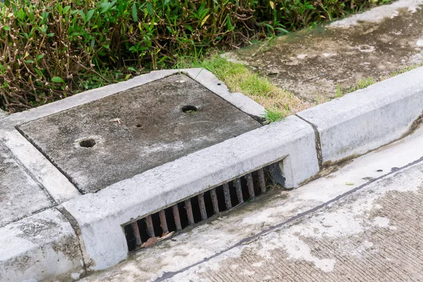 Sewer Drain along Road. A storm drain on the side of a road. Suburban street drain.