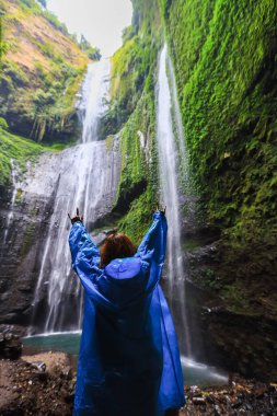 Şelalenin önünde dikilen ve ellerini uzatmış kadının dikiz manzarası. Şelalenin yanında kazanan. Spor ve aktif yaşam konsepti. Seyahat ve özgürlük. Kadın tropikal şelale manzarasından hoşlanıyor.