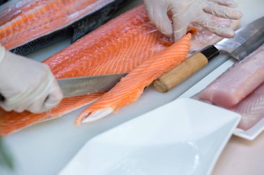 Somon, deneyimli şefin elinde. Sashimi ve suşi için somon filetosu dilimlemek için bıçak kullanıyor. Bir şef somon filetosunu kesme tahtasındaki bıçakla kesiyor. Balık filetosu. 