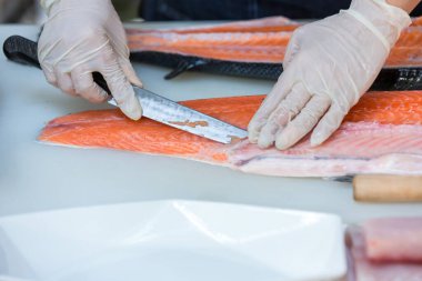 Somon, deneyimli şefin elinde. Sashimi ve suşi için somon filetosu dilimlemek için bıçak kullanıyor. Bir şef somon filetosunu kesme tahtasındaki bıçakla kesiyor. Balık filetosu. 